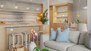 A modern living room with a grey sofa, white cushions, and a dining area with a wooden table and bar.