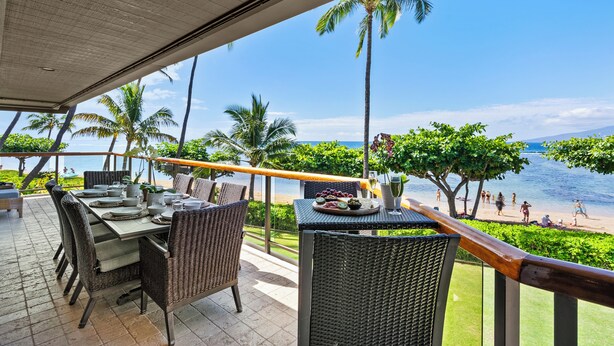 An outdoor dining area with wicker furniture, a table set for a meal, and a view of the beach and ocean.