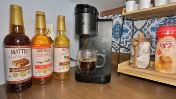 Una encimera de cocina con tres botellas de sirope de café, una cafetera y un cartón de Nestlé Coffee Mute.