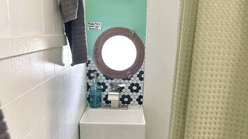 A bathroom with a white sink, a mirror with a brown frame, a towel hanging on the wall, and a sign instructing to turn the water on slowly.