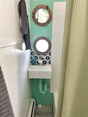 A bathroom with a white sink, a mirror with a brown frame, a towel hanging on the wall, and a sign instructing to turn the water on slowly.