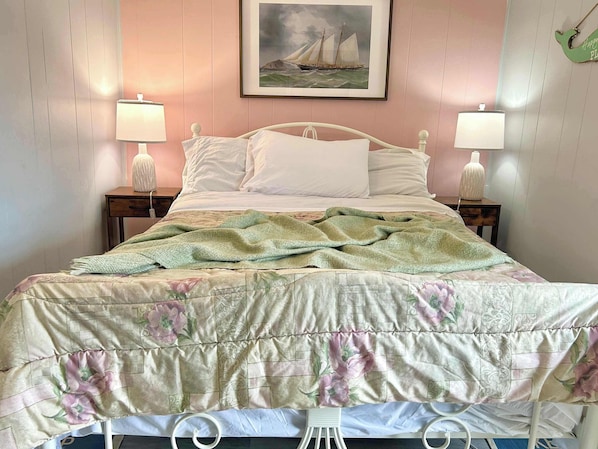 A bed with a floral comforter, two bedside lamps, a framed picture above the bed, and a small table with a lamp beside the bed.