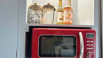 Un four à micro-ondes Galanz rouge, doté d’un écran numérique, d’un panneau de commande et d’un bouton de démarrage. Au-dessus, on trouve trois bocaux en verre avec des couvercles, dont l’un contient un chiffon blanc, et deux bouteilles étiquetées « sirop de café Matteo ».