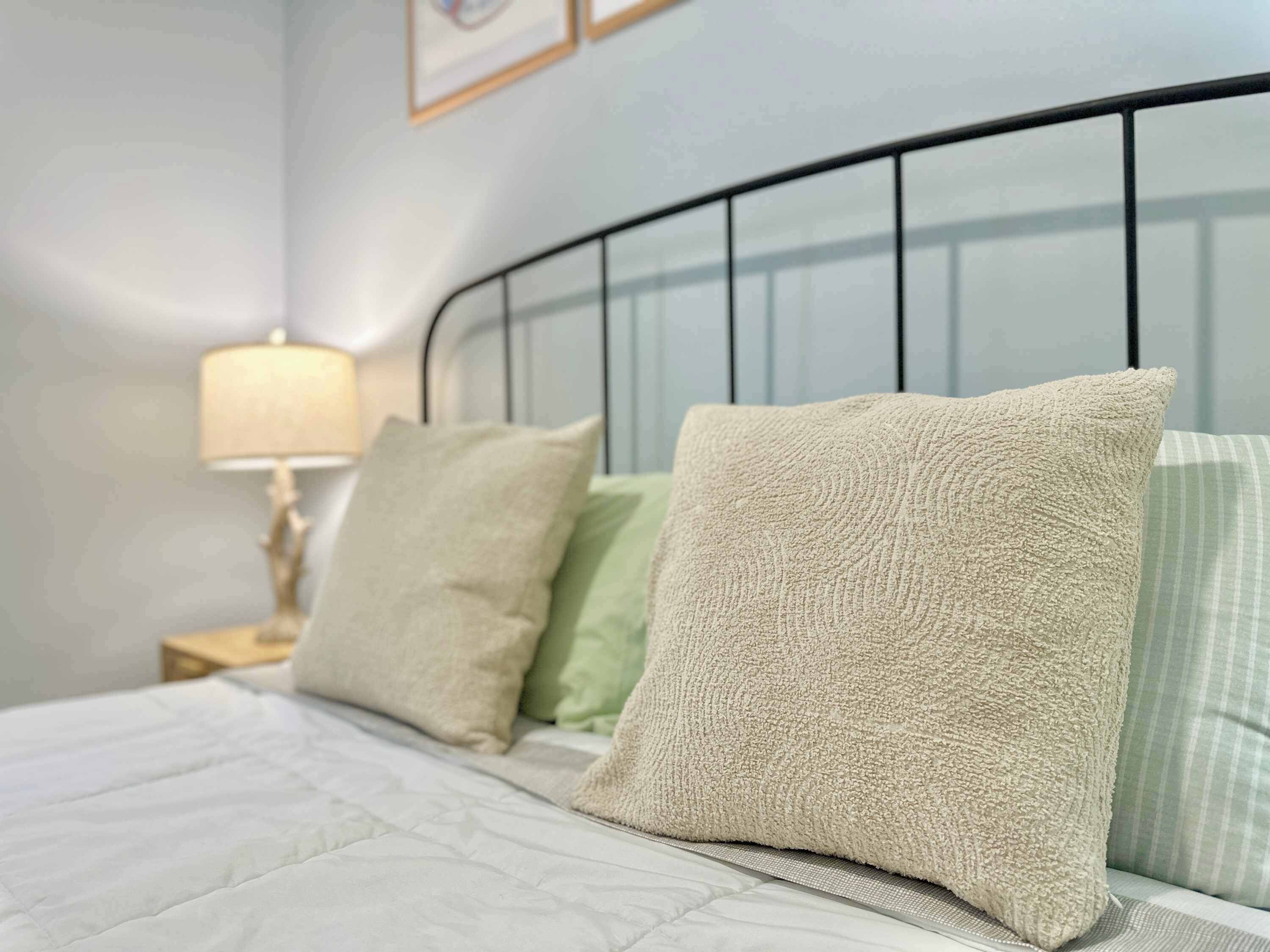 Un lit avec une couette blanche, deux oreillers beiges et un oreiller vert.