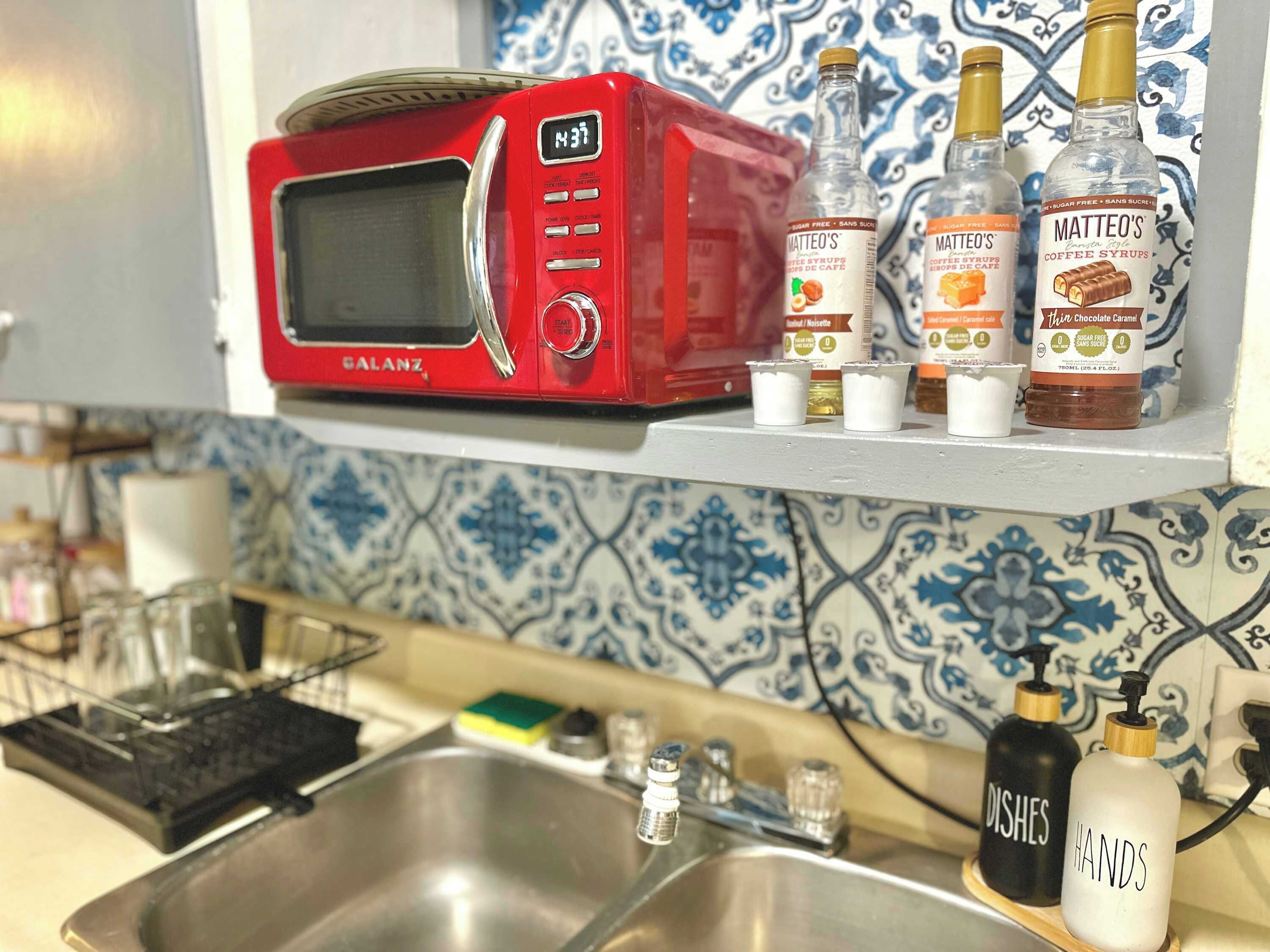 A kitchen with a red Galanz microwave, coffee syrups, and hand sanitizer on the counter.