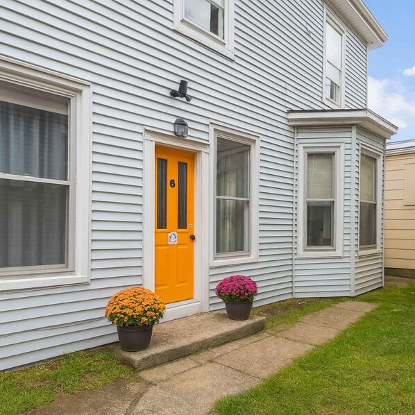 A white house with a yellow door, two windows, and two potted plants.
