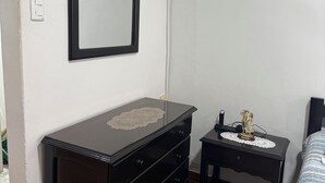 Een slaapkamer met een donkere houten dressoir, een klein nachtkastje met een beeldje, en een bed met een gestreept beddegoed.