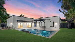 Una casa moderna con piscina, patio y zona de estar exterior cubierta.