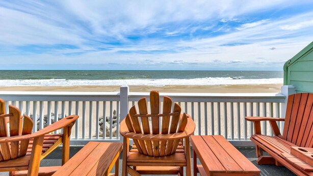 Una terrazza in legno con sedie e tavoli che si affaccia su una spiaggia con onde.