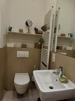 A bathroom with a toilet, sink, towel rack, and shelves with toiletries. - Quiet Altbau 2-Room Apartment with Terrace | Central Berlin near Parks & S-Bahn (Berlin)