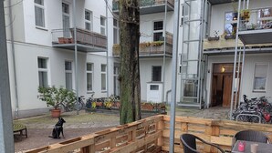 A courtyard with a wooden fence, a tree, and a seating area with a table and chairs. - Quiet Altbau 2-Room Apartment with Terrace | Central Berlin near Parks & S-Bahn (Berlin)