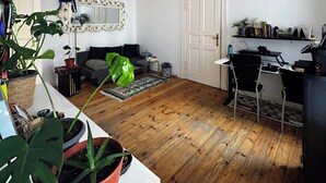 A living room with a wooden floor, a sofa, a coffee table, and a potted plant. - Quiet Altbau 2-Room Apartment with Terrace | Central Berlin near Parks & S-Bahn (Berlin)