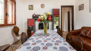 A dining area with a table covered by a patterned tablecloth, surrounded by chairs, and a vase of flowers in the center. - Villa Giulietta - Castiadas (Castiadas)