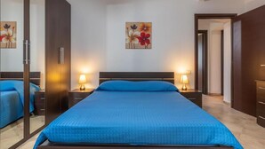 A bedroom with a large bed, two bedside tables with lamps, a mirror, and a wall-mounted artwork. - Villa Giulietta - Castiadas (Castiadas)