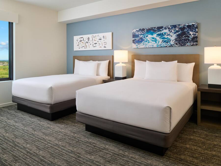 A hotel room with two beds, a large window, and artwork on the walls.