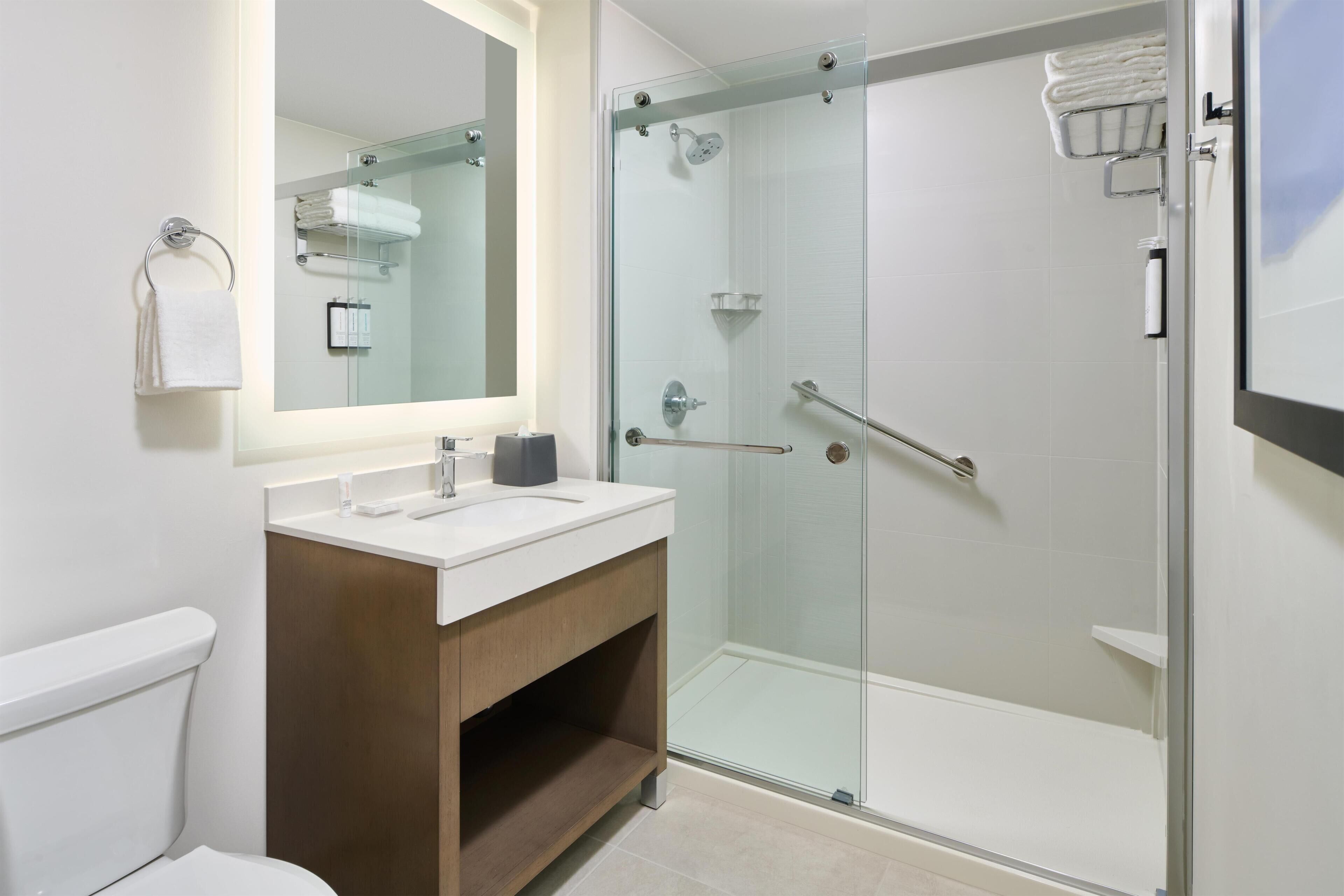 Ein modernes Badezimmer mit einer Glaskabine zur Dusche, einem weißen Waschbecken und einem großen Spiegel.