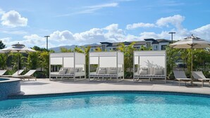 A pool area with lounge chairs and umbrellas, a clear sky, and a residential building in the background. - Hyatt House at Ho'opili (Ewa Beach)