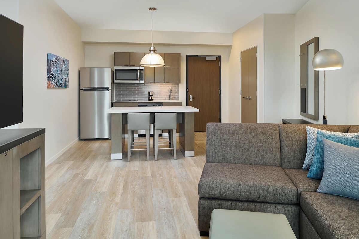Un espacio habitable compacto con kitchenette, sofá, televisor y lámpara colgante.
