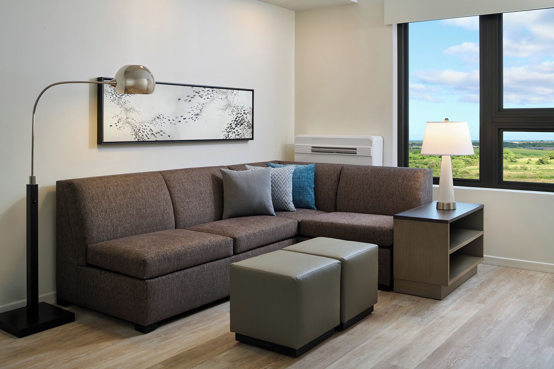 A modern living room with a sectional sofa, a floor lamp, a side table with a lamp, and a large window with a view.