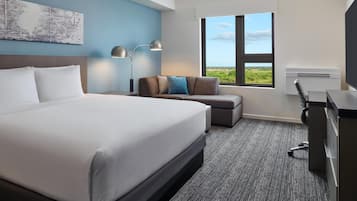 Una habitación de hotel con una cama grande, un escritorio, una silla, un sofá, un ventanal con vistas y una obra de arte colgada en la pared.