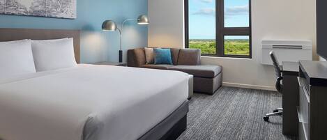 Habitación de hotel con una cama grande, un escritorio, una silla, un sofá, una lámpara y una ventana con vistas.