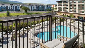 A pool area with lounge chairs and umbrellas, a parking lot, and multi-story buildings in the background. - Hyatt House at Ho'opili (Ewa Beach)