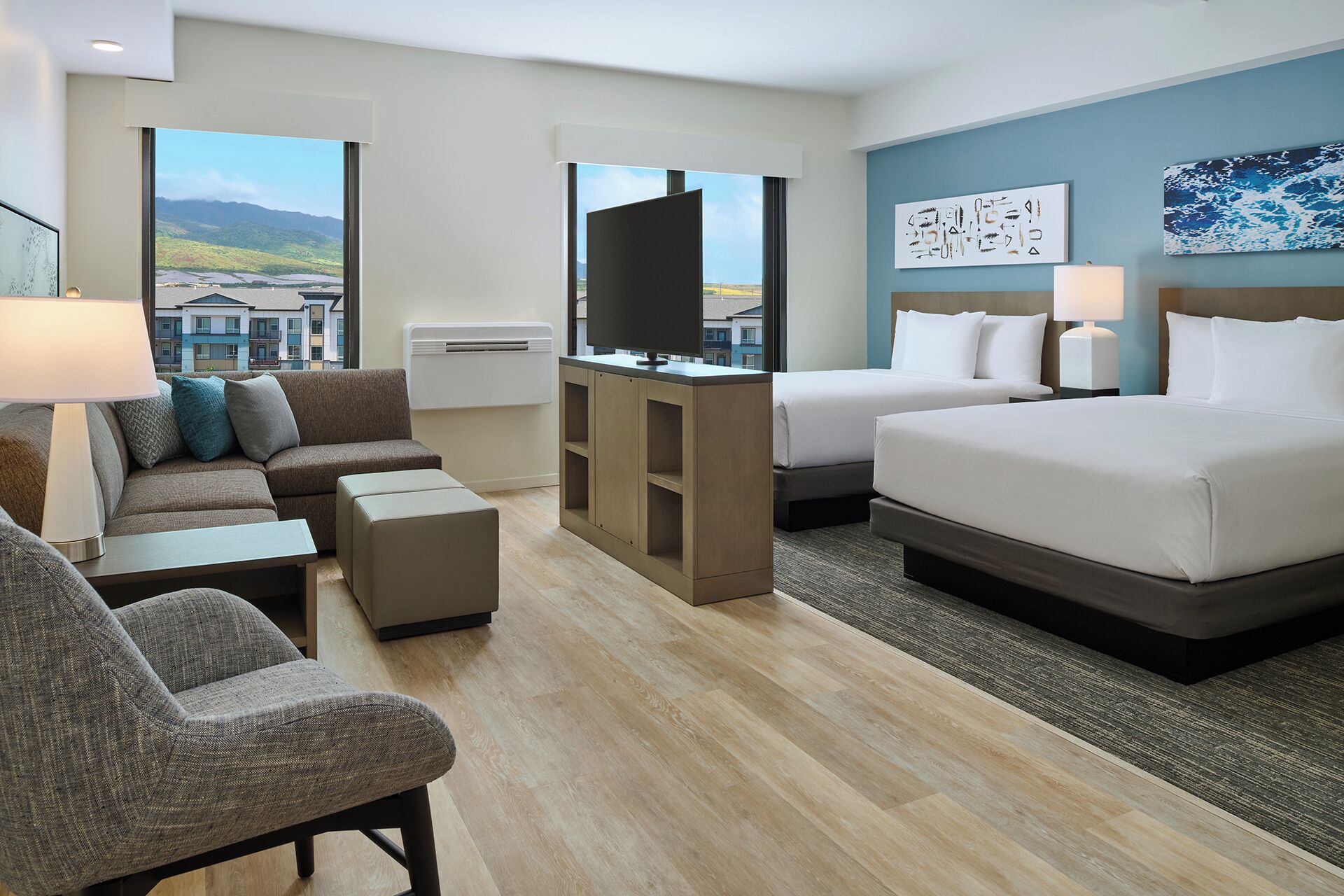 Ein Hotelzimmer mit einer Couch, zwei Betten, einem Fernseher und Blick auf Gebäude.