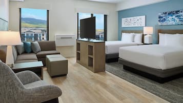 Ein Hotelzimmer mit einer Couch, zwei Betten, einem Fernseher und Blick auf Gebäude.