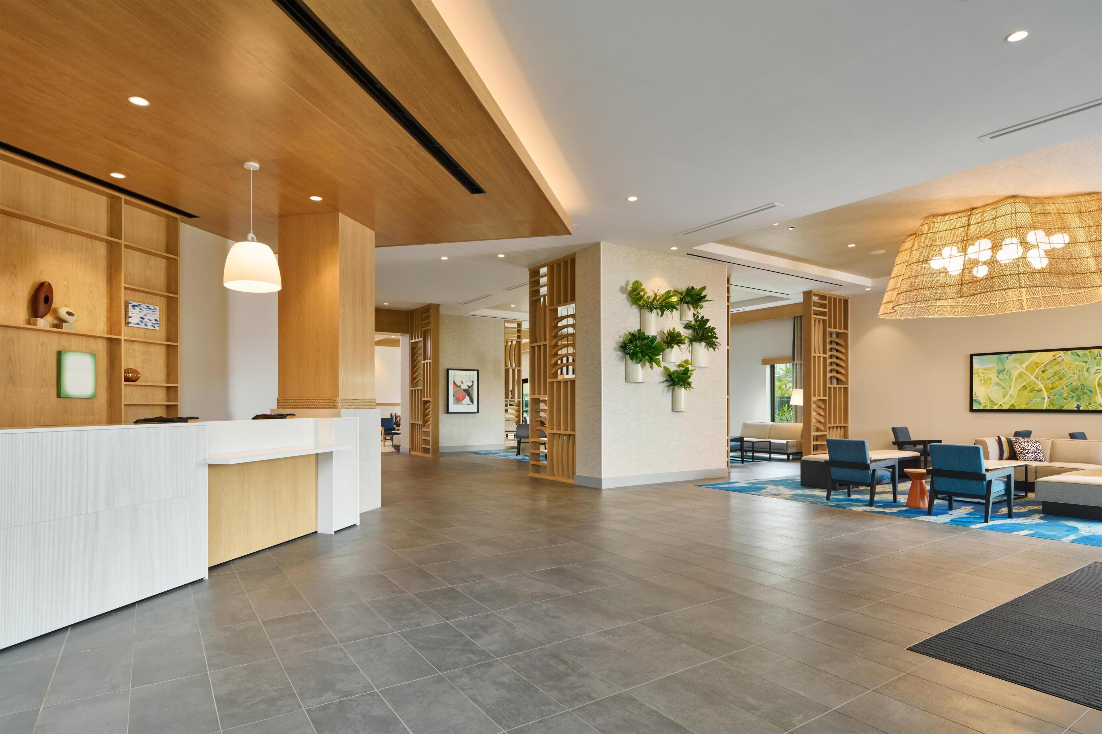 Un área de recepción moderna con un mostrador blanco, estanterías de madera y una lámpara colgante grande.