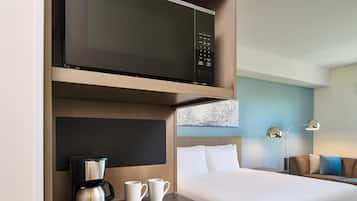 Habitación de hotel con cama, cafetera, dos tazas, microondas y televisor montado en la pared.