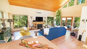 A spacious living room with a fireplace, a blue sofa, and a dining area with a wooden table. - Oak & Vine: Pool | Hot Tub | Fire Table | BBQ (Glen Ellen)