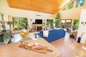 A spacious living room with a fireplace, a blue sofa, and a dining area with a wooden table. - Oak & Vine: Pool | Hot Tub | Fire Table | BBQ (Glen Ellen)