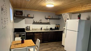 Une cuisine de taille réduite, avec des meubles de rangement en bois foncé, un réfrigérateur blanc et une table à manger en bois accompagnée de deux chaises.