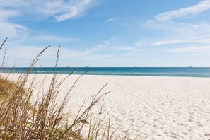 A beach with white sand and sparse grass in the foreground. - Flip Flop Oasis · Hot Tub, Pool & Private Beach Access (Gulf Shores)