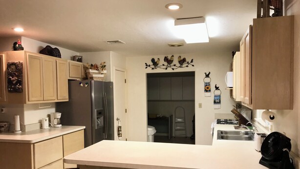 A kitchen with a central island, wooden chairs, a refrigerator, and a microwave.