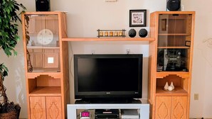 A wooden entertainment center with a flat-screen TV, two speakers, and a shelf with decorative items.
