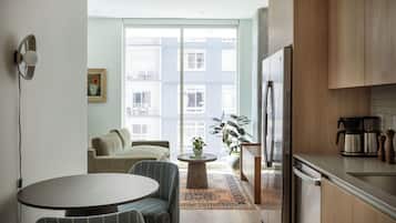 Eine moderne Küche mit Essbereich, einem Kühlschrank, einer Kaffeemaschine und Blick auf ein Gebäude durch das Fenster.