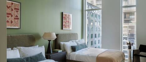 A hotel room with two beds, a nightstand, a lamp, a chair, and a window with a city view.