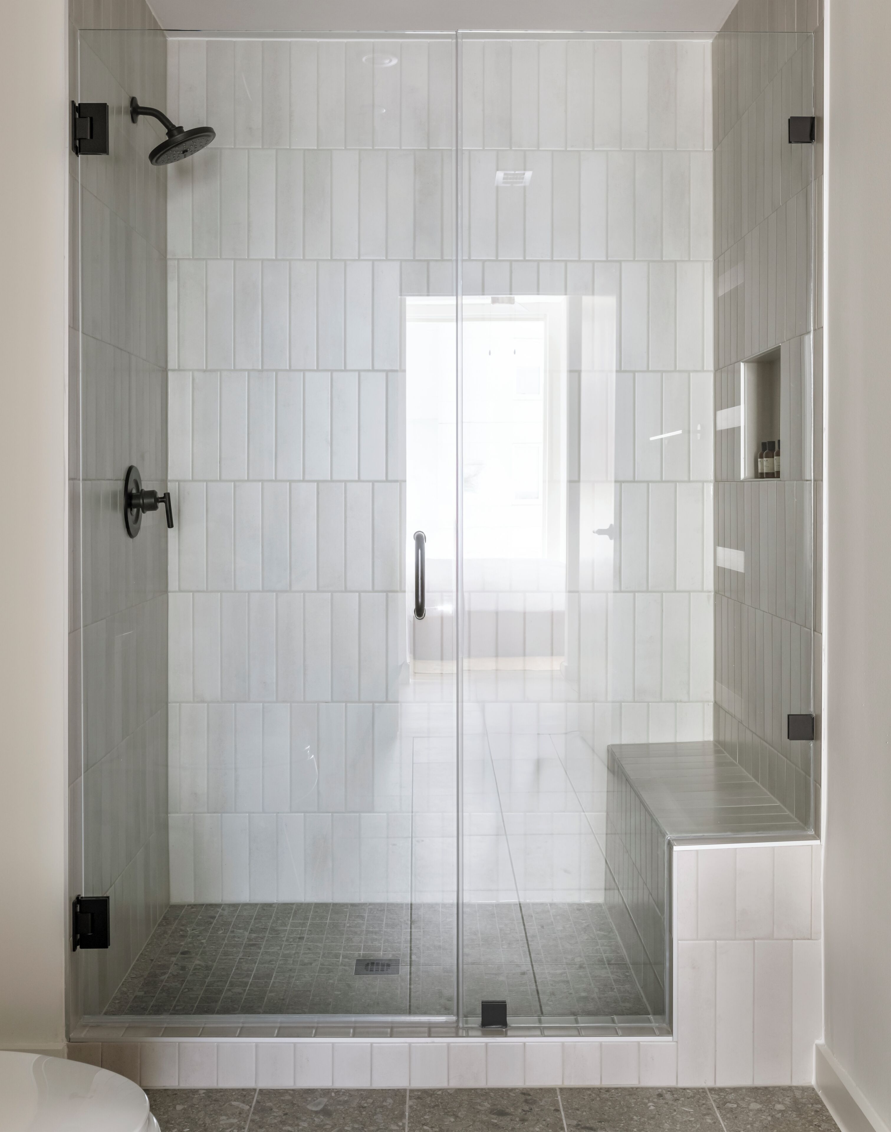 A glass-enclosed shower with a tiled floor and a white wall.