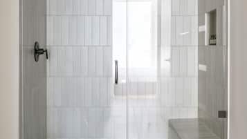 A glass-enclosed shower with a tiled floor and a white wall.
