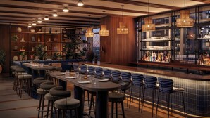 A bar area with a long counter, stools, and shelves with bottles and glasses. - ROOST Rainey (Austin)