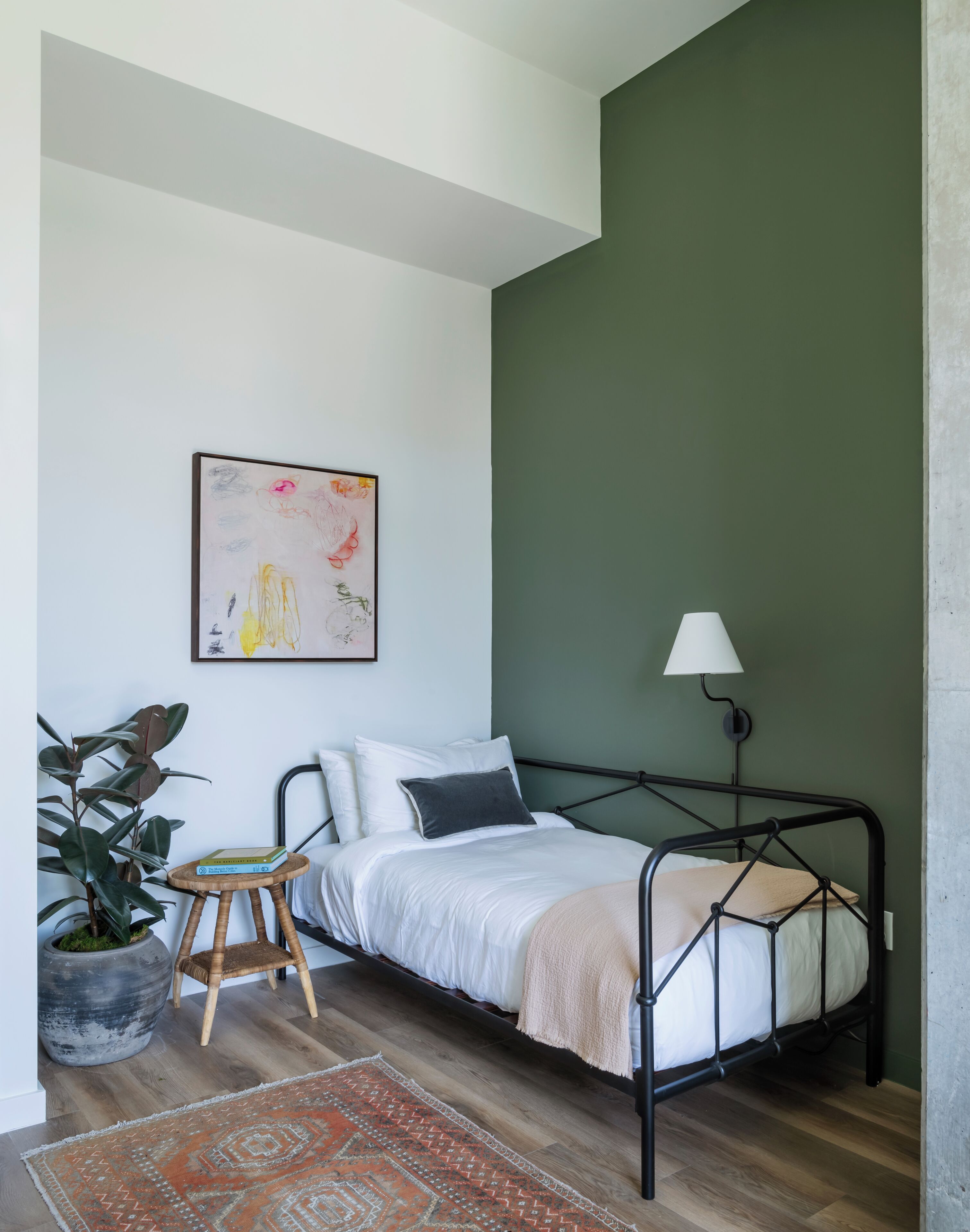 Une chambre à coucher avec un lit, une lampe de chevet, une plante en pot et une œuvre d’art encadrée accrochée au mur.