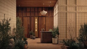 A reception area with a wooden reception desk, potted plants, and a neon sign reading "AYA". - ROOST Rainey (Austin)