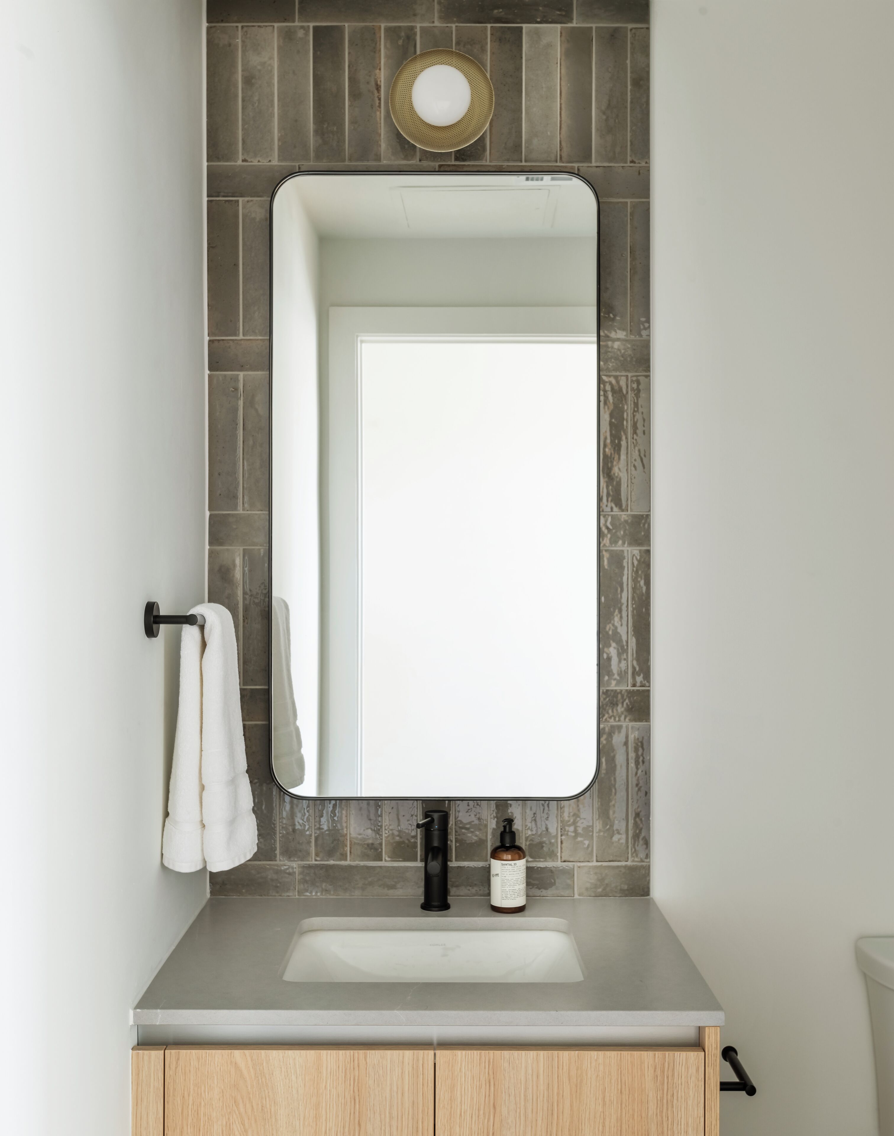 A bathroom with a rectangular mirror, a sink, a towel rack, and a soap dispenser.