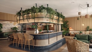 A bar area with a curved counter, bar stools, and a seating area with a green sofa and wicker chairs. - ROOST Rainey (Austin)