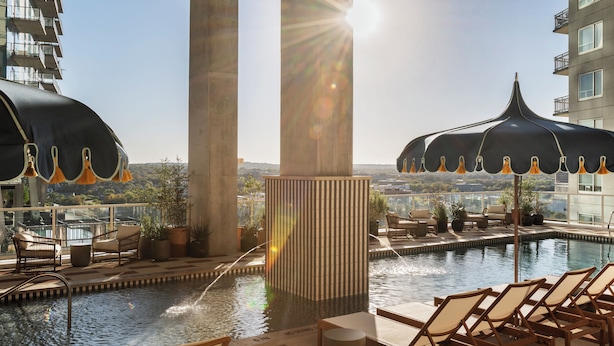 A rooftop pool area with lounge chairs, a water feature, and a view of the cityscape. - ROOST Rainey (Austin)