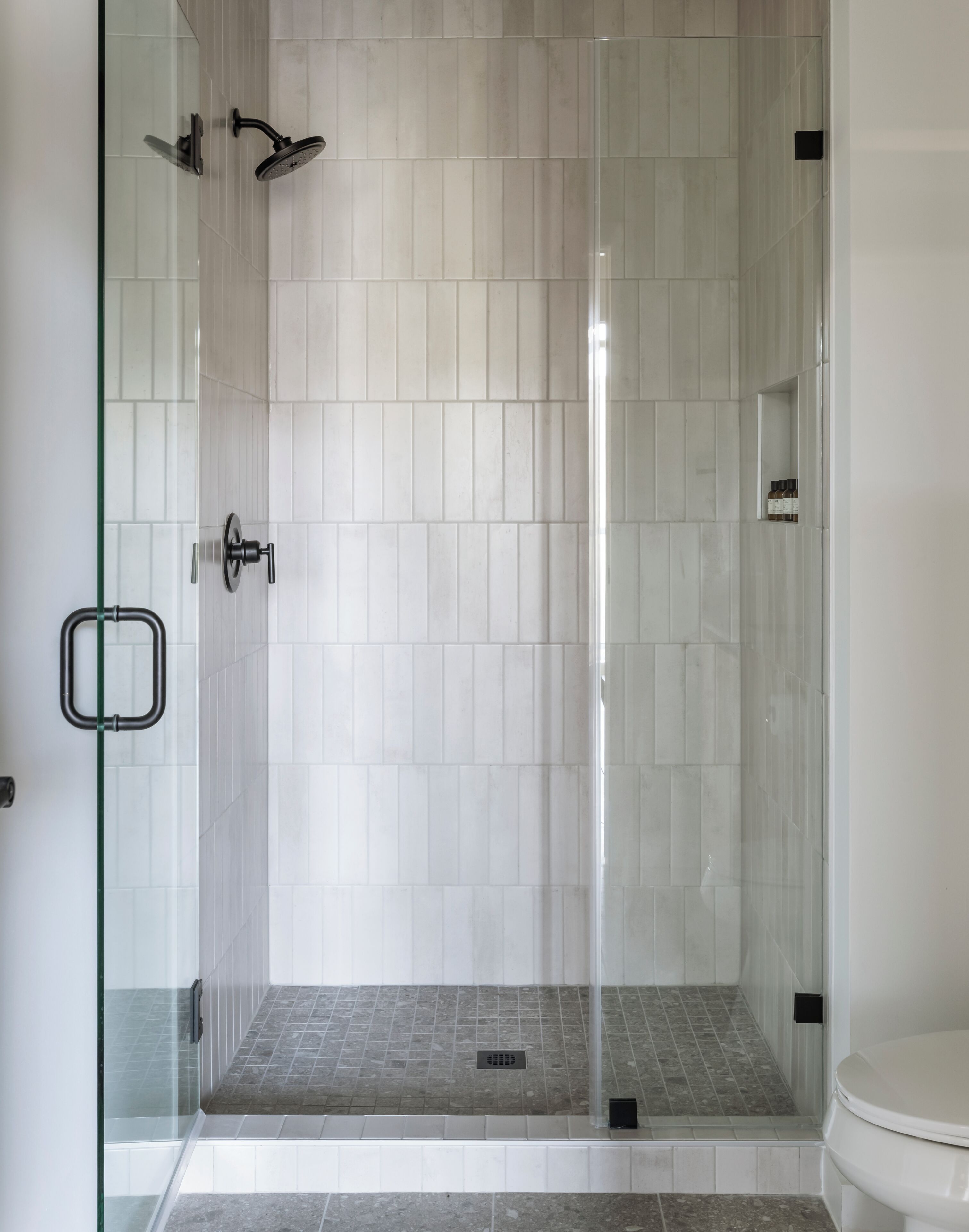 A shower with a glass door, a white tiled wall, and a tiled floor.