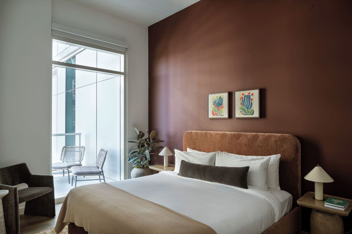 Una habitación de hotel moderna con una cama grande, una zona de estar con sillas, una planta en maceta y obras de arte en la pared.