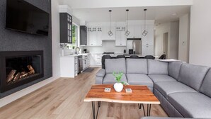Un salon moderne avec un canapé d’angle gris, une table basse en bois et une cheminée.
