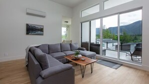 Un salon moderne avec un canapé d’angle gris, une table basse en bois et de grandes fenêtres donnant sur un paysage montagneux.